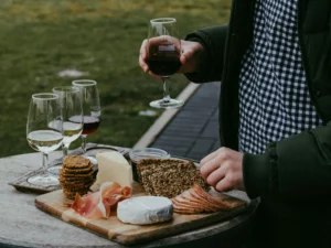 trois verres de vin sur une table avec plateau de fromages et charcuterie et main tenant un verre